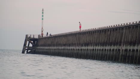 hombre en traje de neopreno salta del muelle al agua