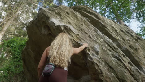 female rock climber standing below large boulder moments before her climb