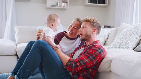 Young-white-couple-sit-playing-with-baby-at-home,-side-view