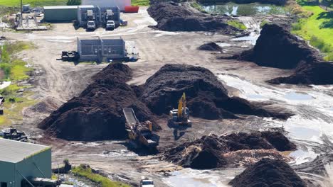drone footage captures an excavator moving soil in an industrial area with piles of dirt and machinery