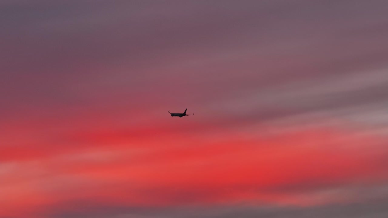 large cargo plane flying through bright pink fluffy clouds at sunset telephoto aerial