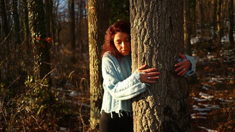 young red hair caucasian girl hugs a tree in the woods at sunset, close up shot, mother nature love concept