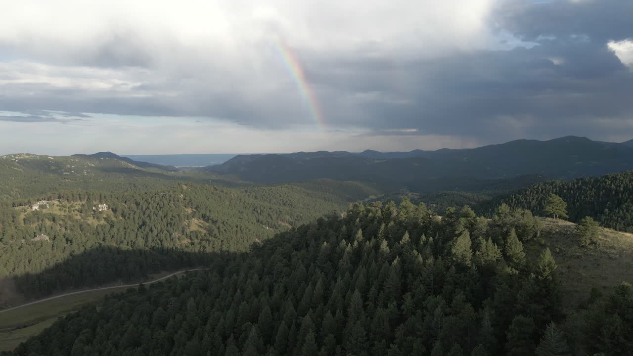 arco iris sobre montañas boscosas con densos árboles de coníferas en colorado, estados unidos