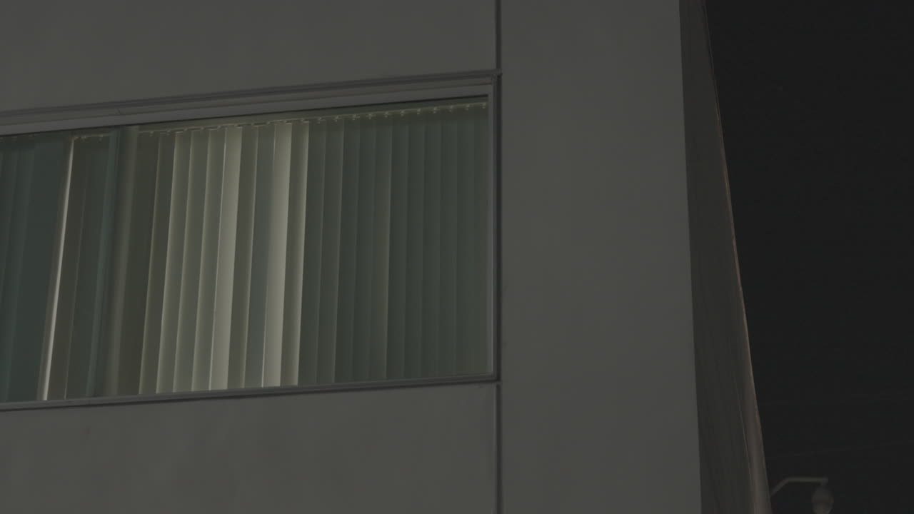 Close up shots of the white apartment building's square window with closed blinds at night
