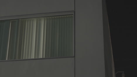 close up shots of the white apartment building's square window with closed blinds at night