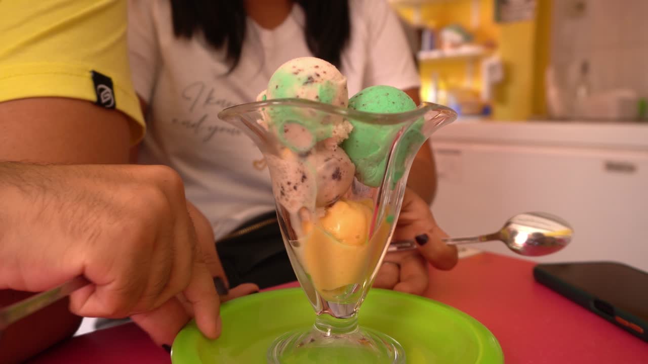 primer plano de varias bolas de helado verdes, amarillas, rojas y blancas en una taza de vidrio