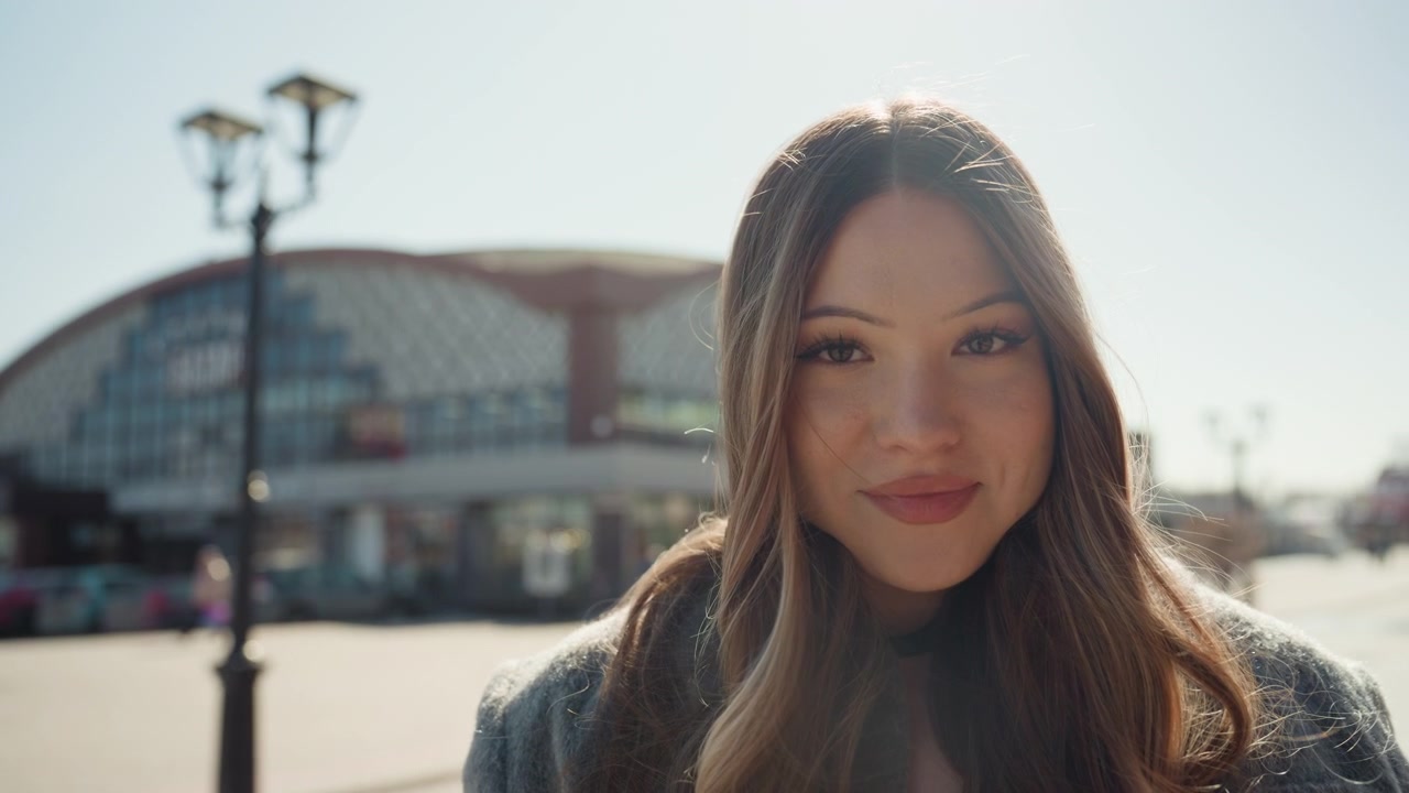 Donna asiatica sorridente che sistema le cuffie all'aperto. Ritratto casuale di donna asiatica in piazza con le cuffie. Donna asiatica rilassata in un ambiente di mercato, che indossa una giacca comoda e con un'espressione coinvolgente