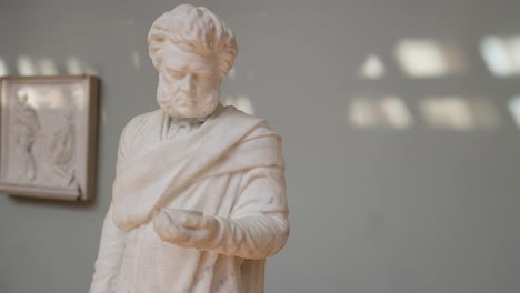 estatua de mármol en postura contemplativa, en el entorno de un museo