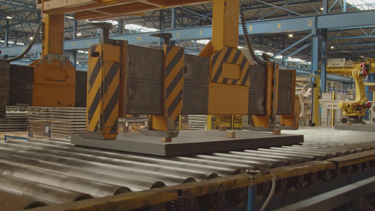 A crane moves over a stack of steel plates on a roller bench