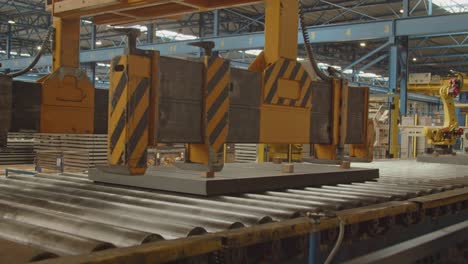 a crane moves over a stack of steel plates on a roller bench