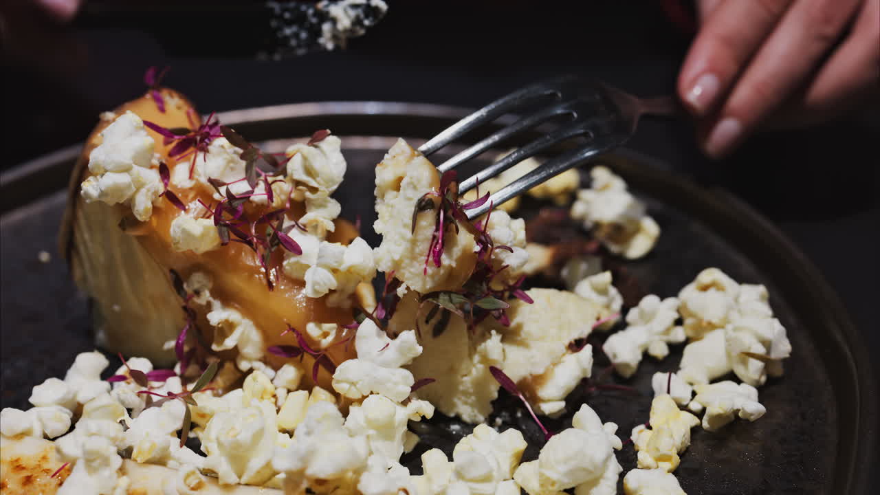 Close up of a woman cutting a cheesecake with a banana split and caramelised popcorn on a black plate at a restaurant