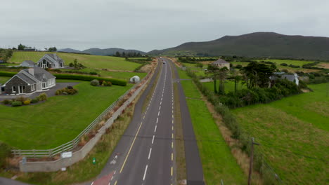 Forwards-fly-above-road-and-cycling-paths-passing-around-detached-houses-in-countryside.-Aerial-landscape-shot.-Ireland