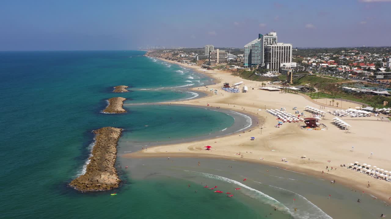 Waves roll out over the beautiful tourist sandy beaches with the large high hotels right on the beach on the bays behind the stone breakwaters in the Mediterranean Sea. Drone dolly shot