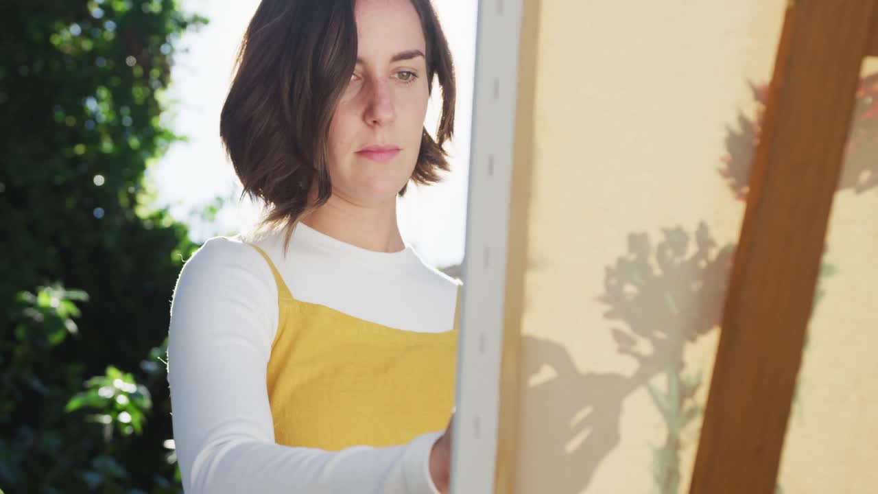 mujer caucásica con cabello marrón pintando en un jardín soleado