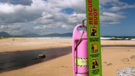 Rosa-Rettungsboje-Am-Strand-Mit-Blauer-Flagge-Von-Kleinmond,-Schöner-Tag-Neben-Der-Lagune