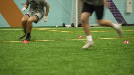 football players running through a drill on turf with cones, wide receivers