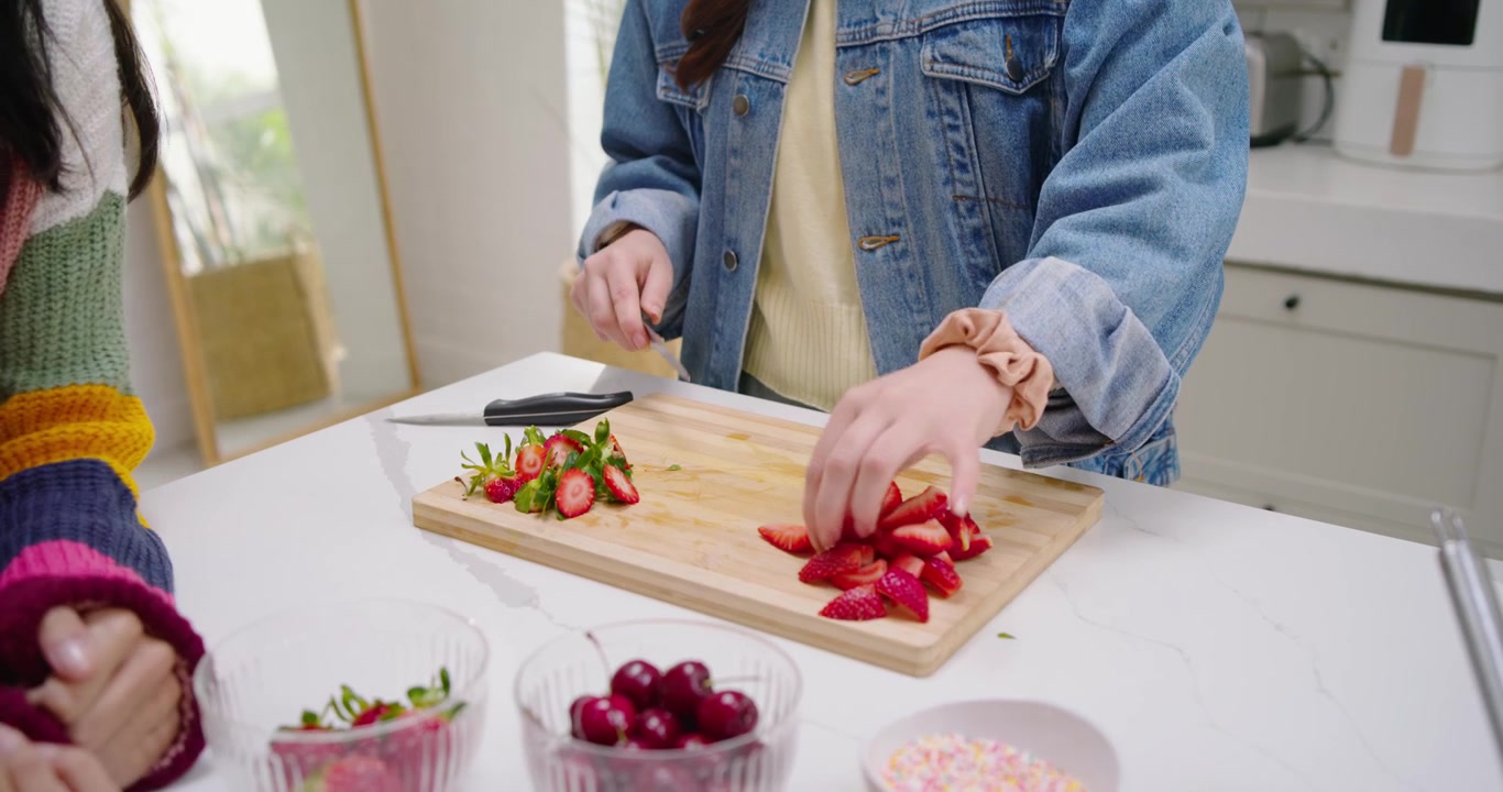 Knife being picked up is slicing strawberries into wedges on cutting board for topping dessert