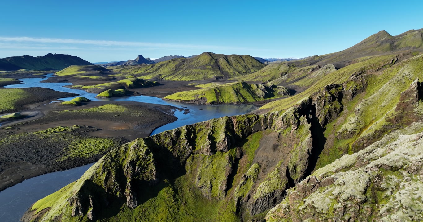 Aerial view of Iceland highlands canyon with mossy volcanic cliffs and winding river, bright blue sky over remote wilderness for travel and adventure background.