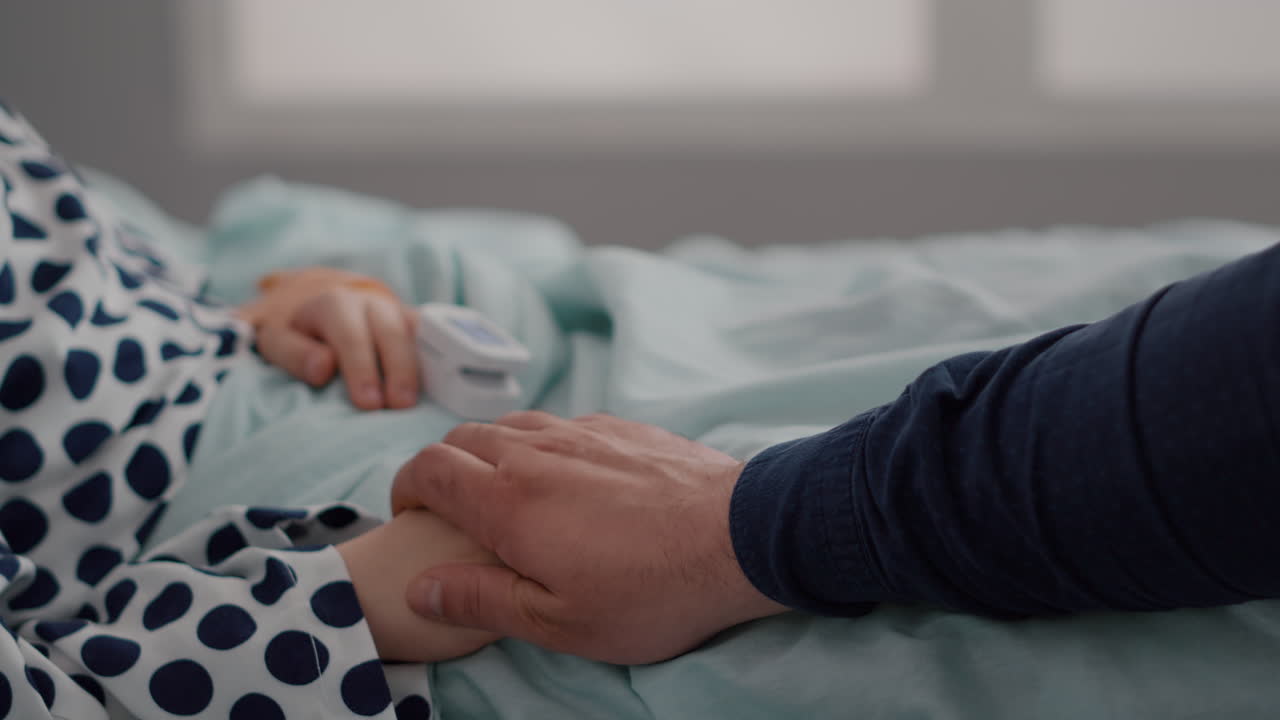 ベッドで休んでいる病気の子供のクローズアップ。指には、心拍数をモニタリングするオキシメーターが装着されています。