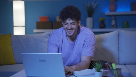 Young-college-student-looking-at-laptop-at-night-and-smiling.