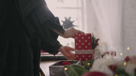 una joven empaca un regalo de navidad en papel rojo y lo ata con cintas.