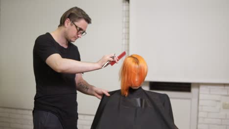 Stylish-professional-male-hairdresser-in-glasses-combing-hair-of-female-client-in-hair-salon-turning-around-her-chair-and