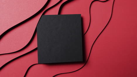 video of close up of square of black paper on waves cut out and copy space on red background