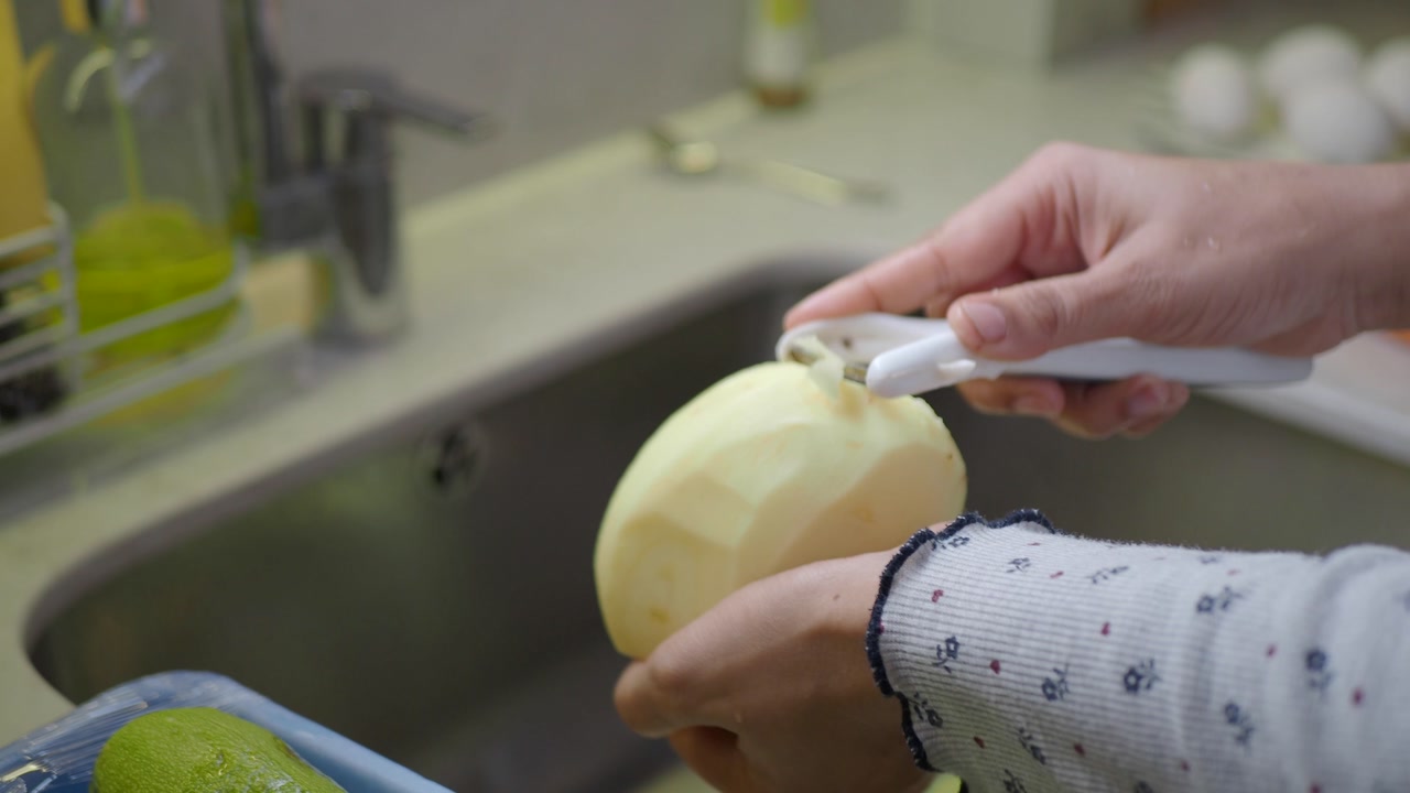 Hands Peeling and Washing a Potato in Kitchen Sink