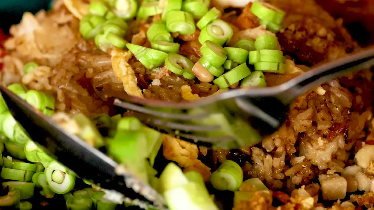 Close-up of fried rice being garnished with fresh vegetables and herbs for added flavor.