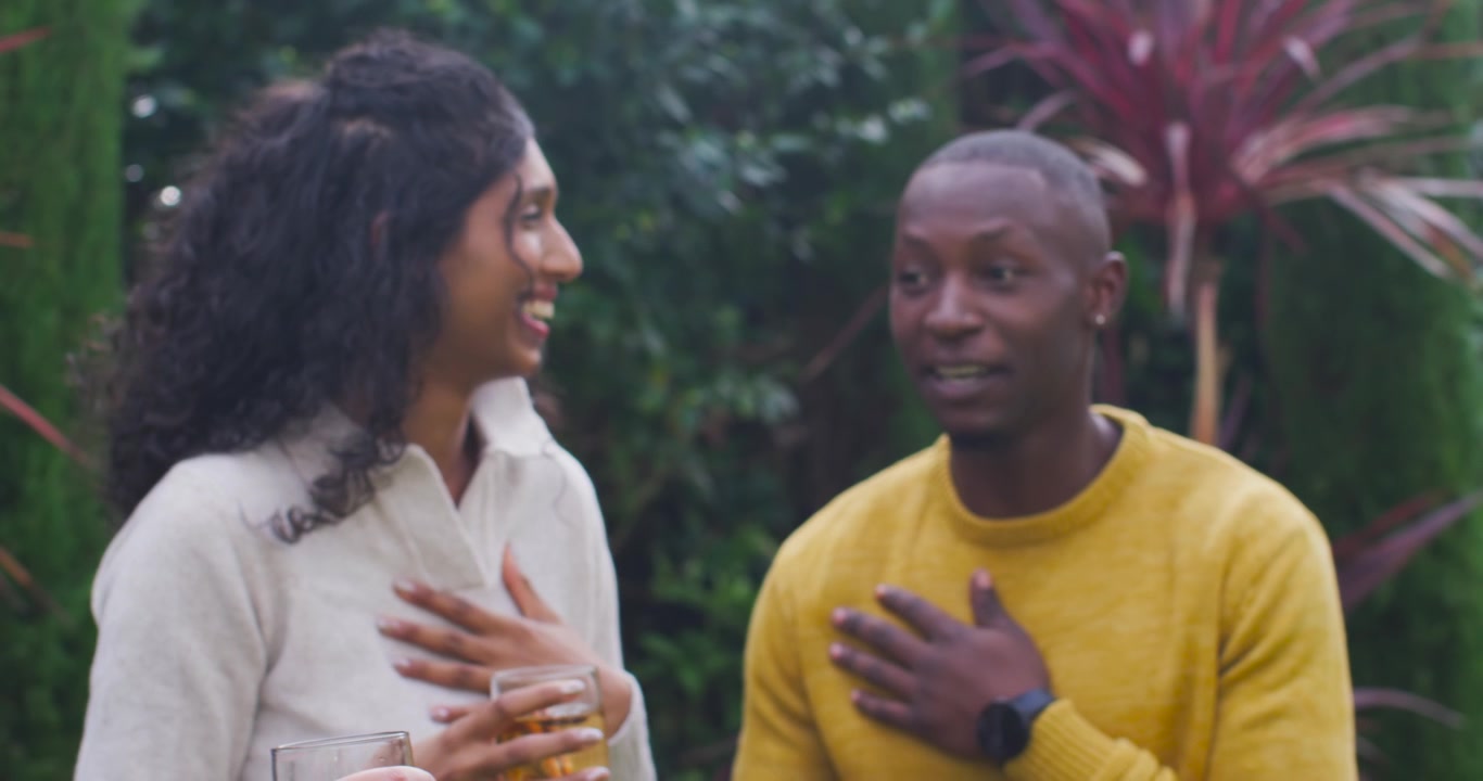 Garden friends curly woman playfully tugging scrunchie, woman sipping glass, man in yellow laughing