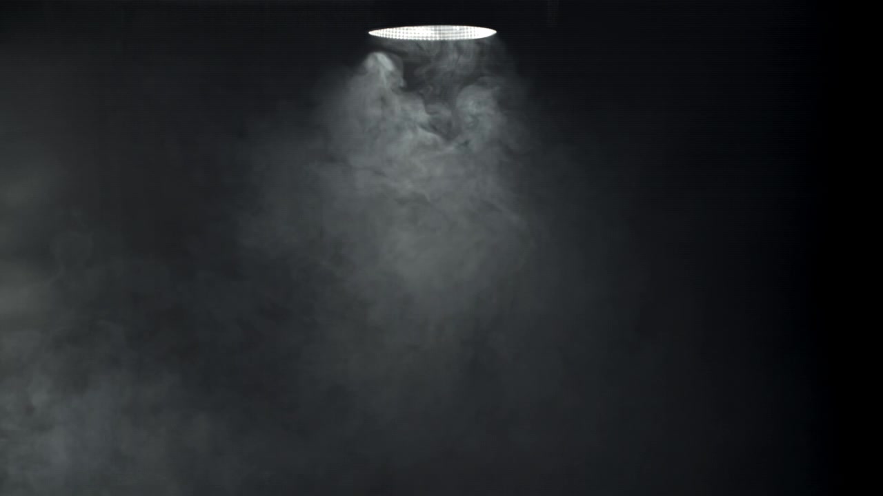 Unico faretto che illumina fumo vorticoso su sfondo scuro