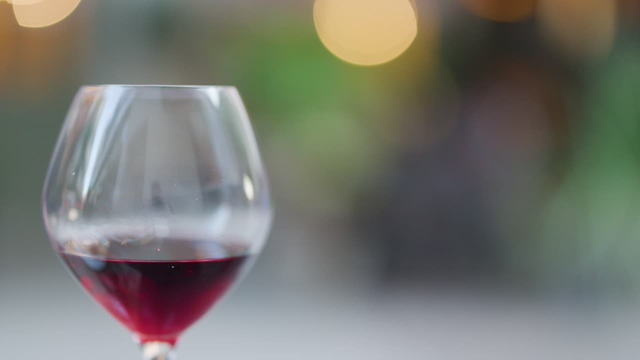 Red wine glass in sharp focus, blurred dining background, gentle camera movement, soft ambient lighting