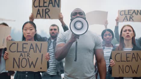 a diverse group advocating for environmental justice, hold signs demanding clean air and rallying together for a sustainable future while one leader speaks passionately