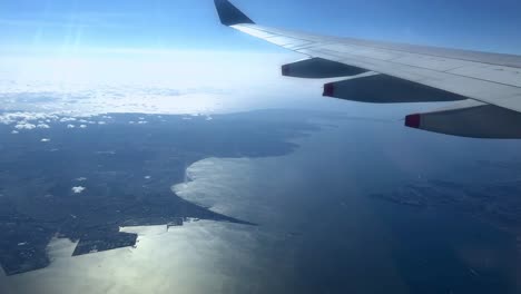 aerial view from airplane window, wing over coastline with blue sky