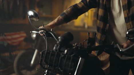 Close-up-a-bike-guy-in-a-checkered-shirt-takes-out-a-repaired-motorcycle-from-his-studio-workshop