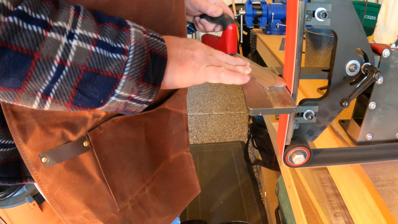 hombre que usa una amoladora de correa para dar forma a la barra de acero en un cuchillo - cierre aislado