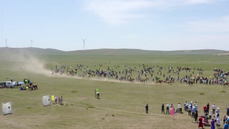 Horse-Riders-Going-Fast-With-Long-Dust-Behind,-Windmills-In-Background