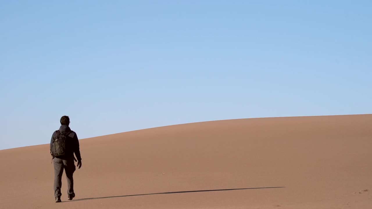 мужчина идет по песчаным дюнам в замедленной съемке