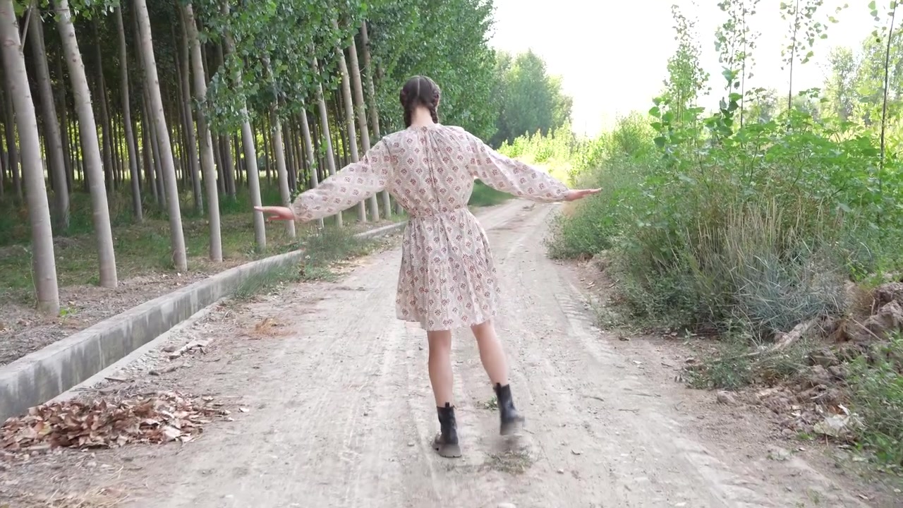 Una giovane donna vestita con un bellissimo abito floreale passeggia felicemente lungo un sentiero alberato.