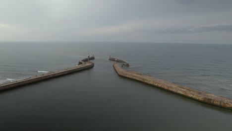 Aerial-shot-of-the-east-and-west-piers-at-the-entrance-to-the-seaside-town-of-Whitby-in-Yorkshire,-Northern-England