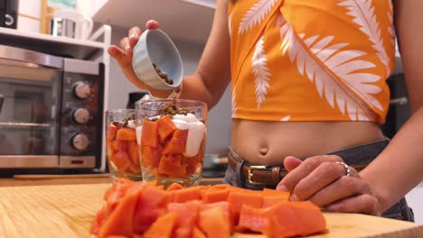mujer preparando un parche de papaya en capas con granola y yogur