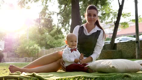 cute baby in suit and bow tie with mommy sitting on green lawn at nature