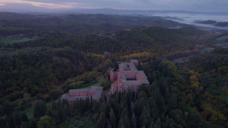 Abbey-of-Monte-Oliveto-Maggiore-red-brick-building-in-forest-landscape-Italy,-aerial