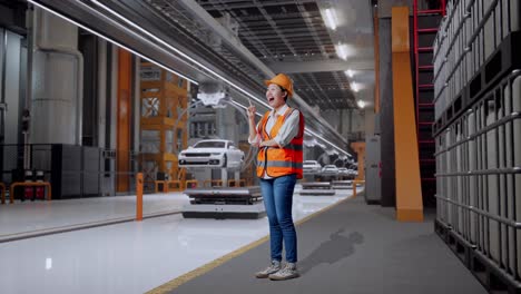 vista lateral completa del cuerpo de una ingeniera asiática con casco de seguridad pensando y mirando a su alrededor y luego levantando su dedo índice mientras estaba de pie en la fábrica de automóviles ev