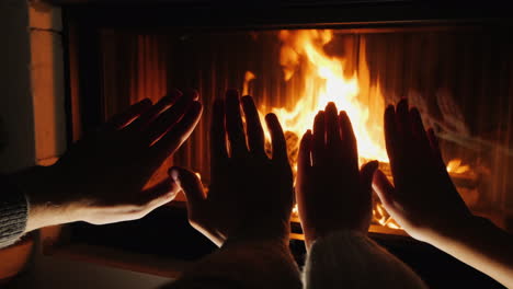 young couple warms their hands by the fireplace romantic evening together