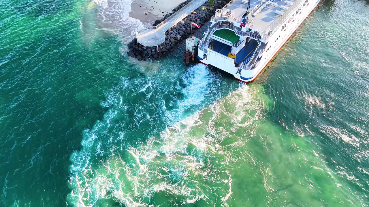 Aerial footage of a ferry docking at Bellarine Peninsula, showcasing turquoise waters and dynamic wave patterns under bright sunlight