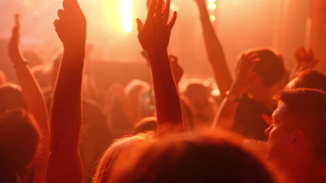 Energetic concert crowd waving heart signs, capturing memorable moments with phones while showing passionate enthusiasm during live music performance