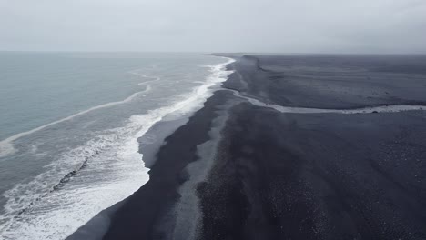 Volando-Sobre-La-Costa-Sur-De-Islandia-Mientras-Las-Olas-Del-Océano-Atlántico-Rompen-En-La-Arena-Negra