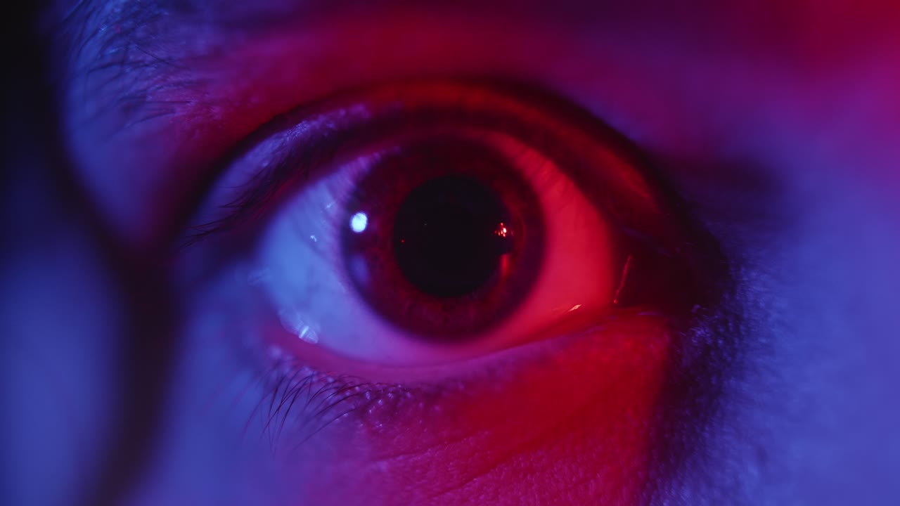 Occhio umano che batte le palpebre sotto intensa illuminazione al neon rossa e blu