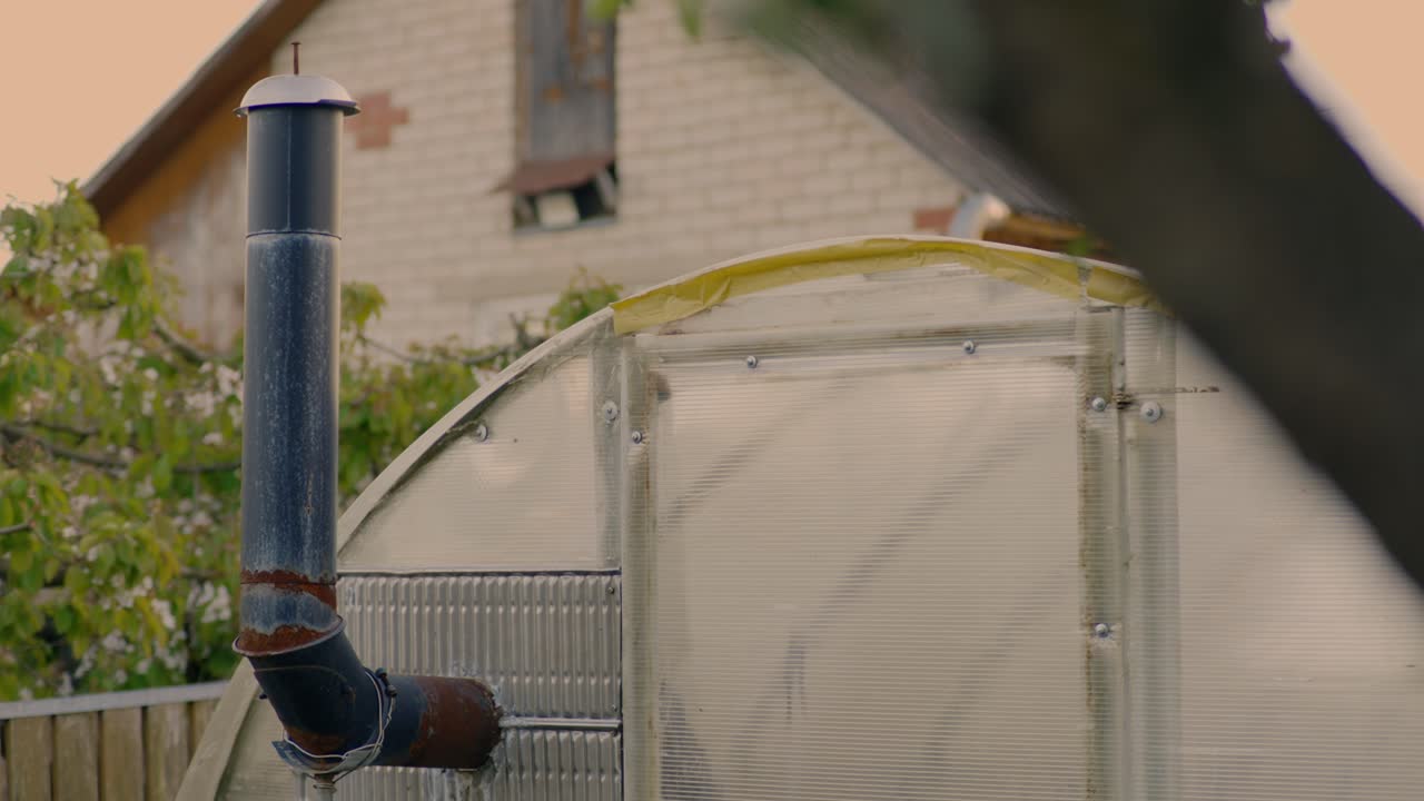 Rusty pipe connected to a polycarbonate greenhouse in a garden